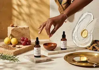 Sorano Organics face oils on marble tiles with raw argan nuts, grapes, and a wooden bowl, highlighting natural oils for african skin glow.